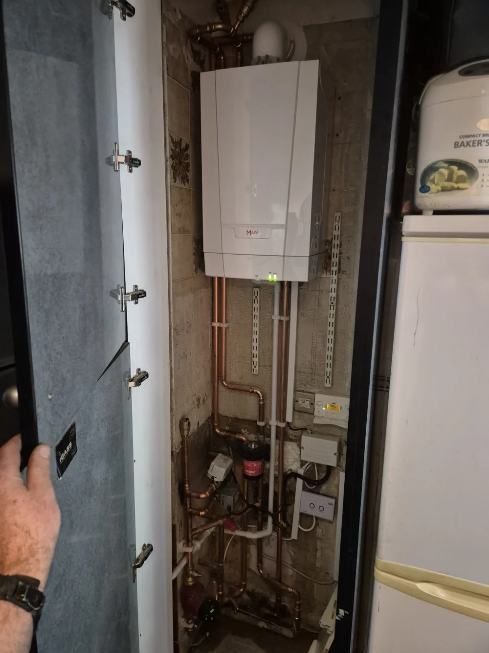 Boiler controls and copper pipework inside a utility cupboard