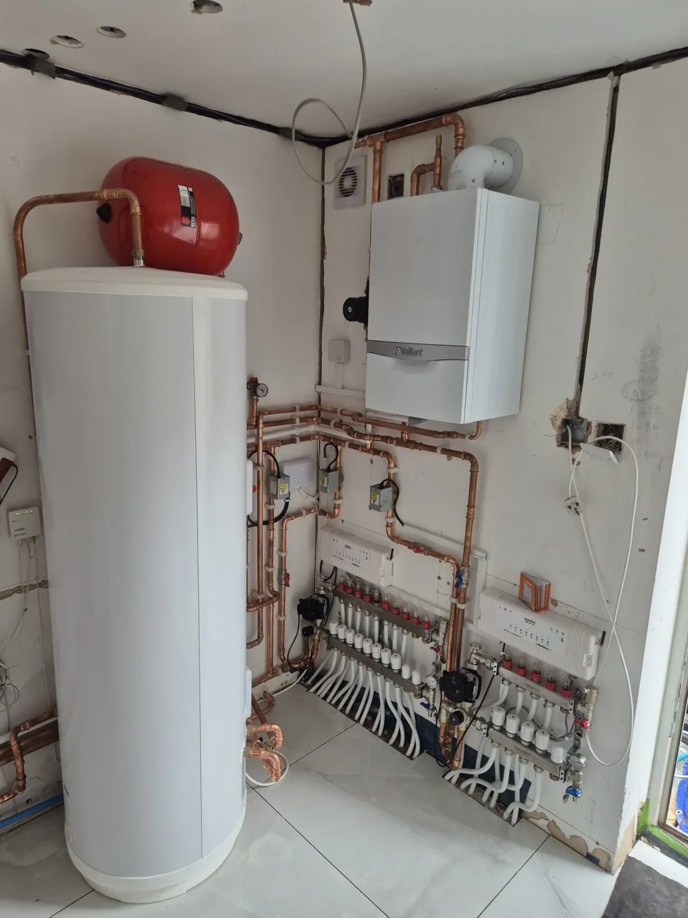 Hot water cylinder beside a heating manifold and copper pipework