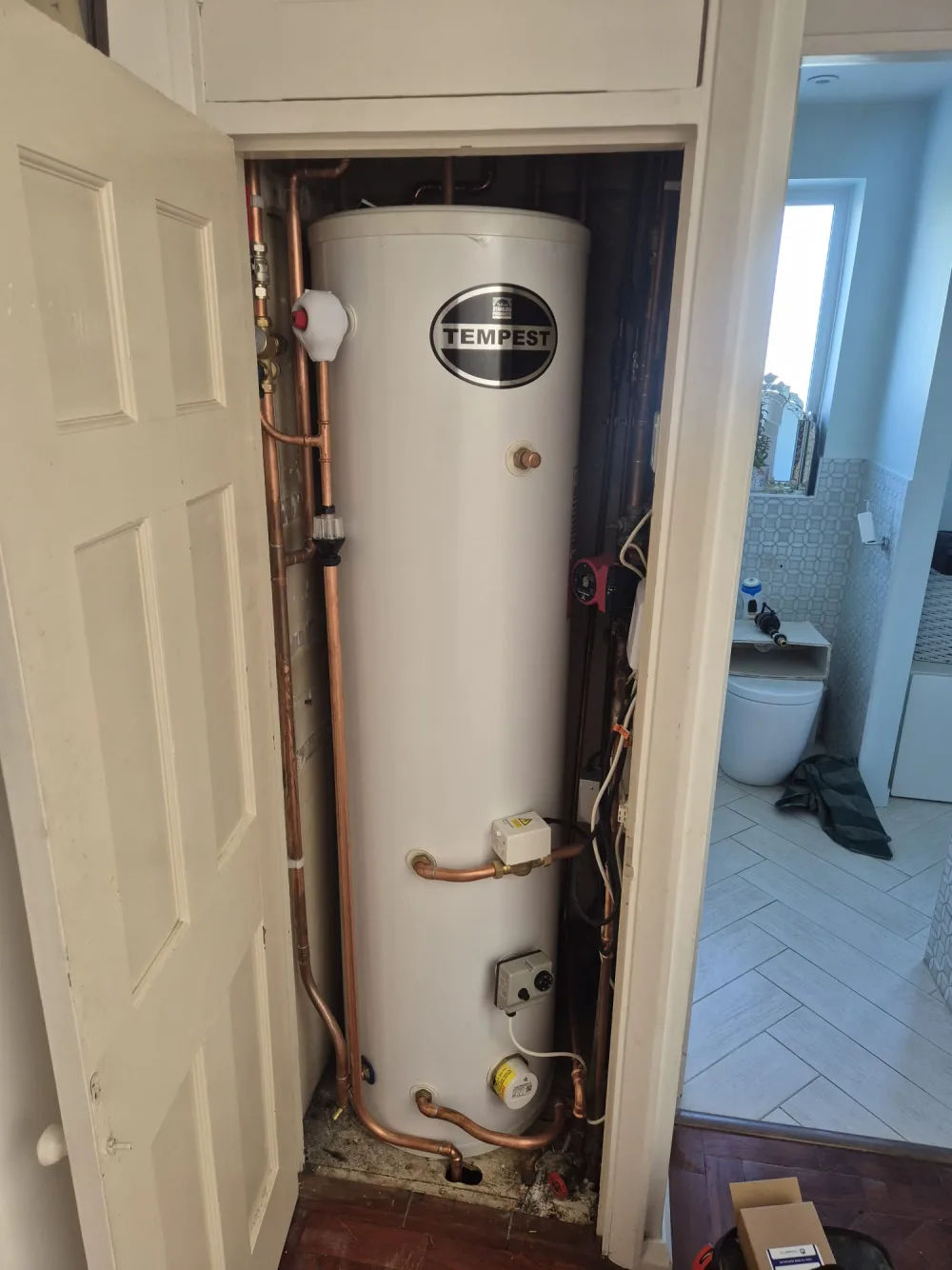 Hot water cylinder and copper pipework in a domestic cupboard